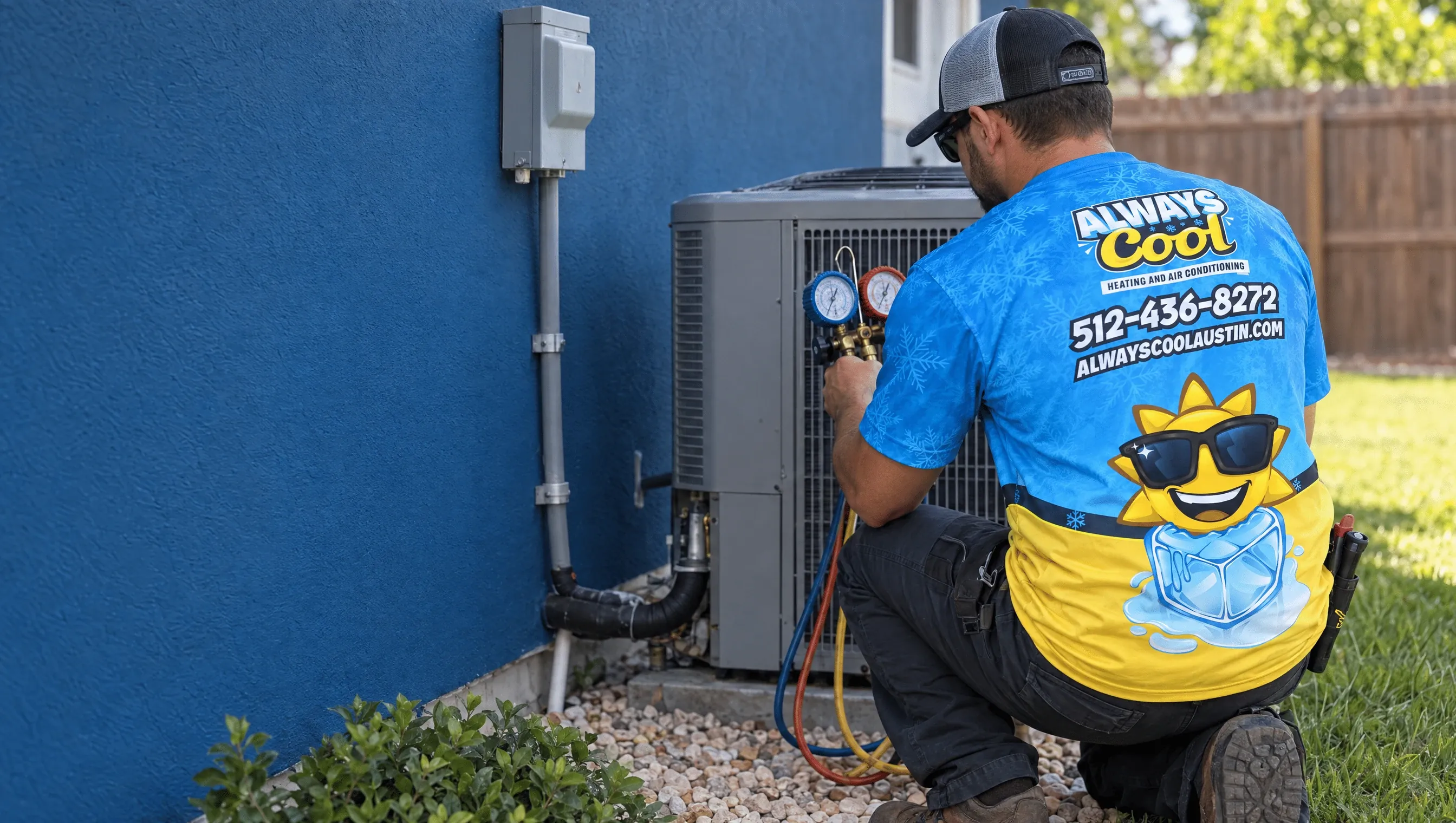 A technician viewed from behind in a blue-and-yellow Always Cool shirt checking refrigerant gauges beside an outdoor air-conditioning condenser against a blue house wall.